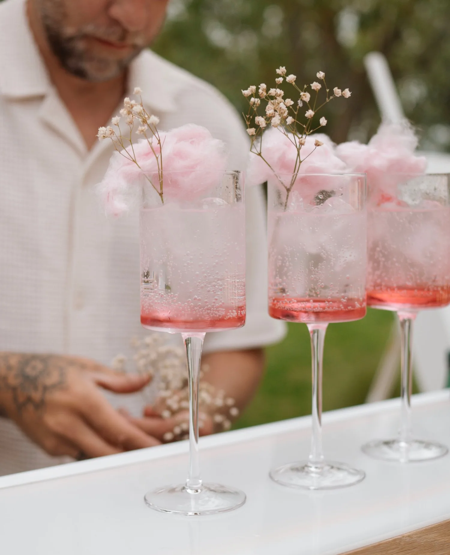 Barman devant trois cocktails surmontés de barbe à papa rose et de gypsophile