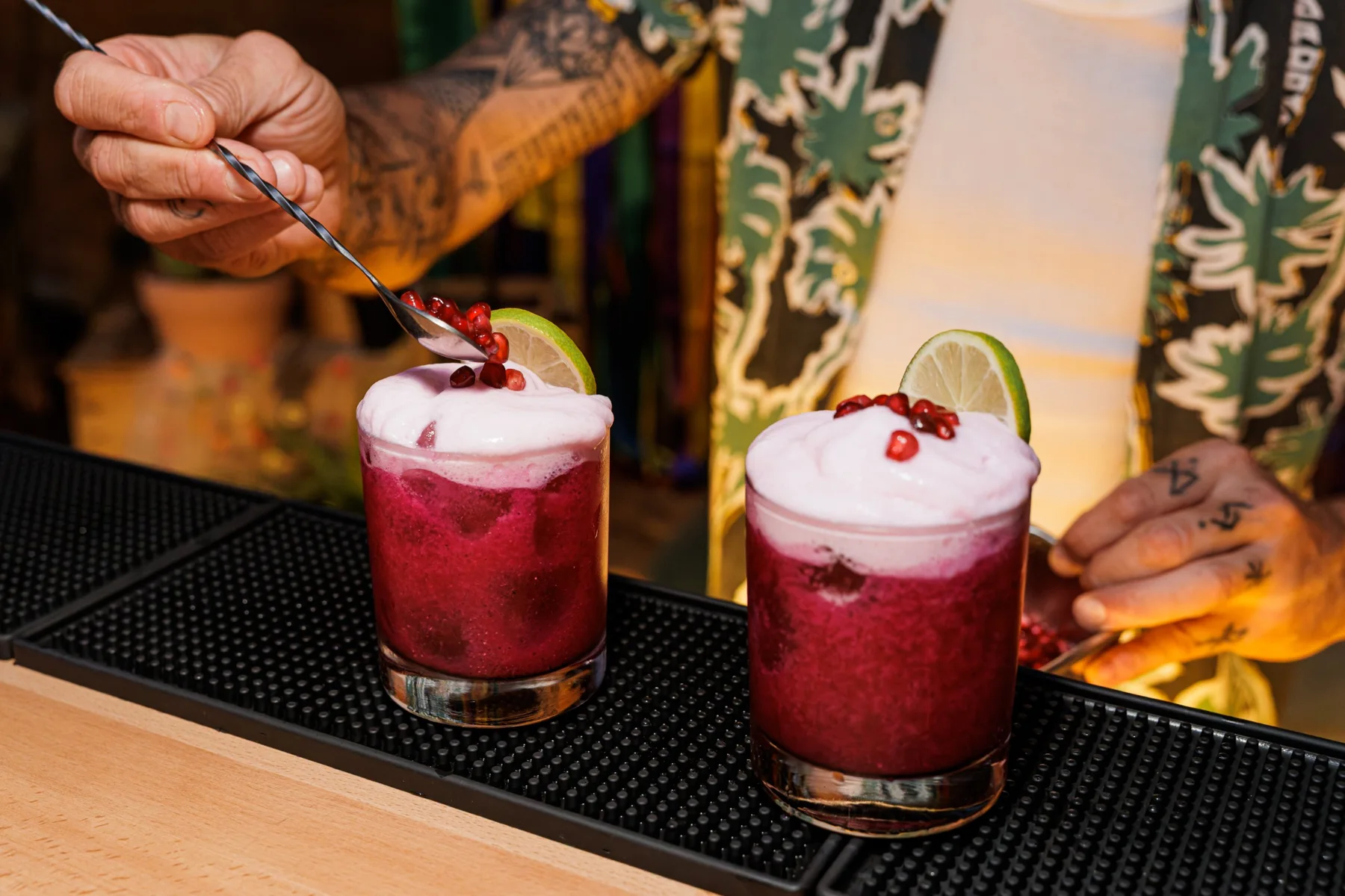 Barman déposant des grains de grenade sur deux cocktails à la mousse rose